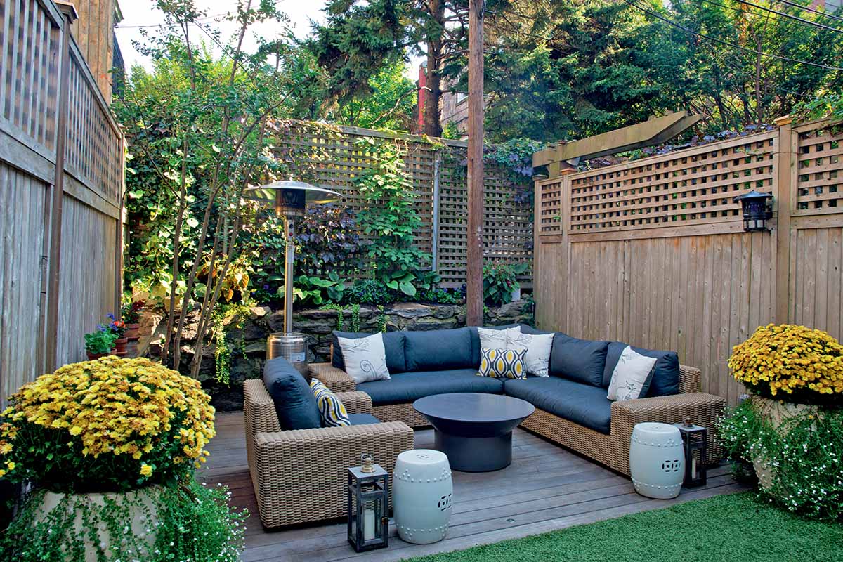 A horizontal image of an enclosed deck with rattan furniture, an outdoor heat lamp, and brightly colored plantings.