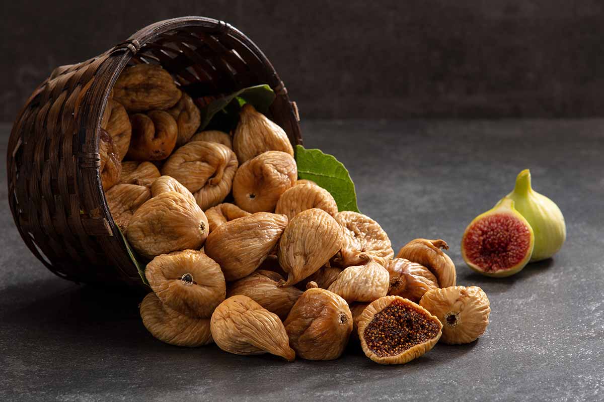 A horizontal image of a basket with dried figs spilling out onto a gray surface.
