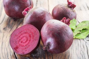 A close up horizontal image of deep red beetroots freshly harvested and cleaned and set on a wooden surface.