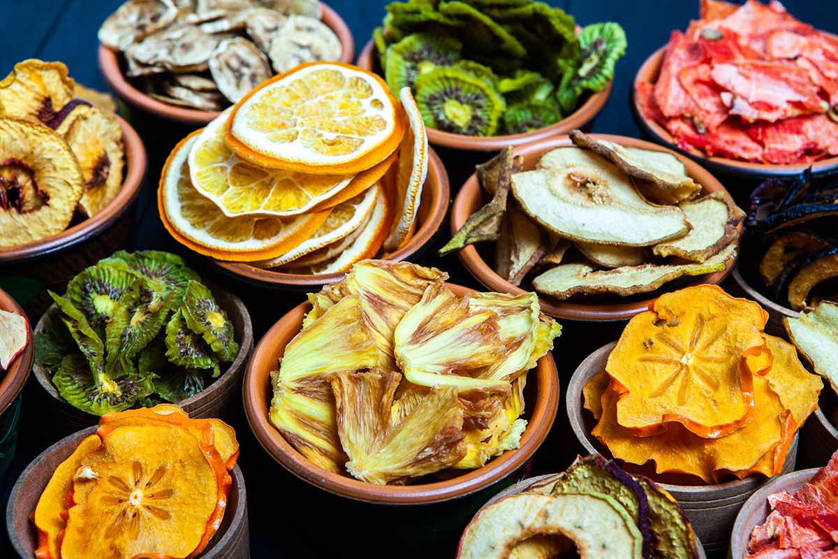 A close up horizontal image of a variety of different fruits and vegetables all dehydrated for easy storage, in separate small bowls.