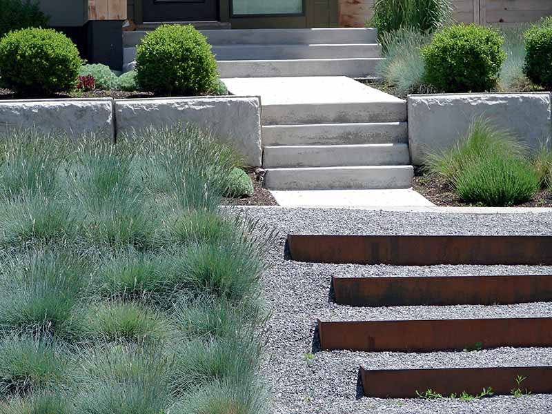 A horizontal image of steps leading up to a residence with ornamental grasses and gravel.