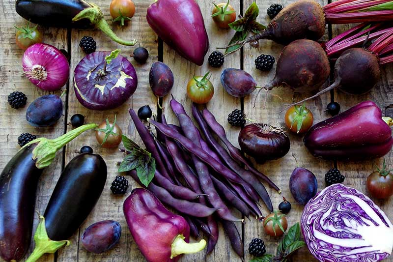 A close up of a variety of different purple vegetables and fruits set on a wooden surface.